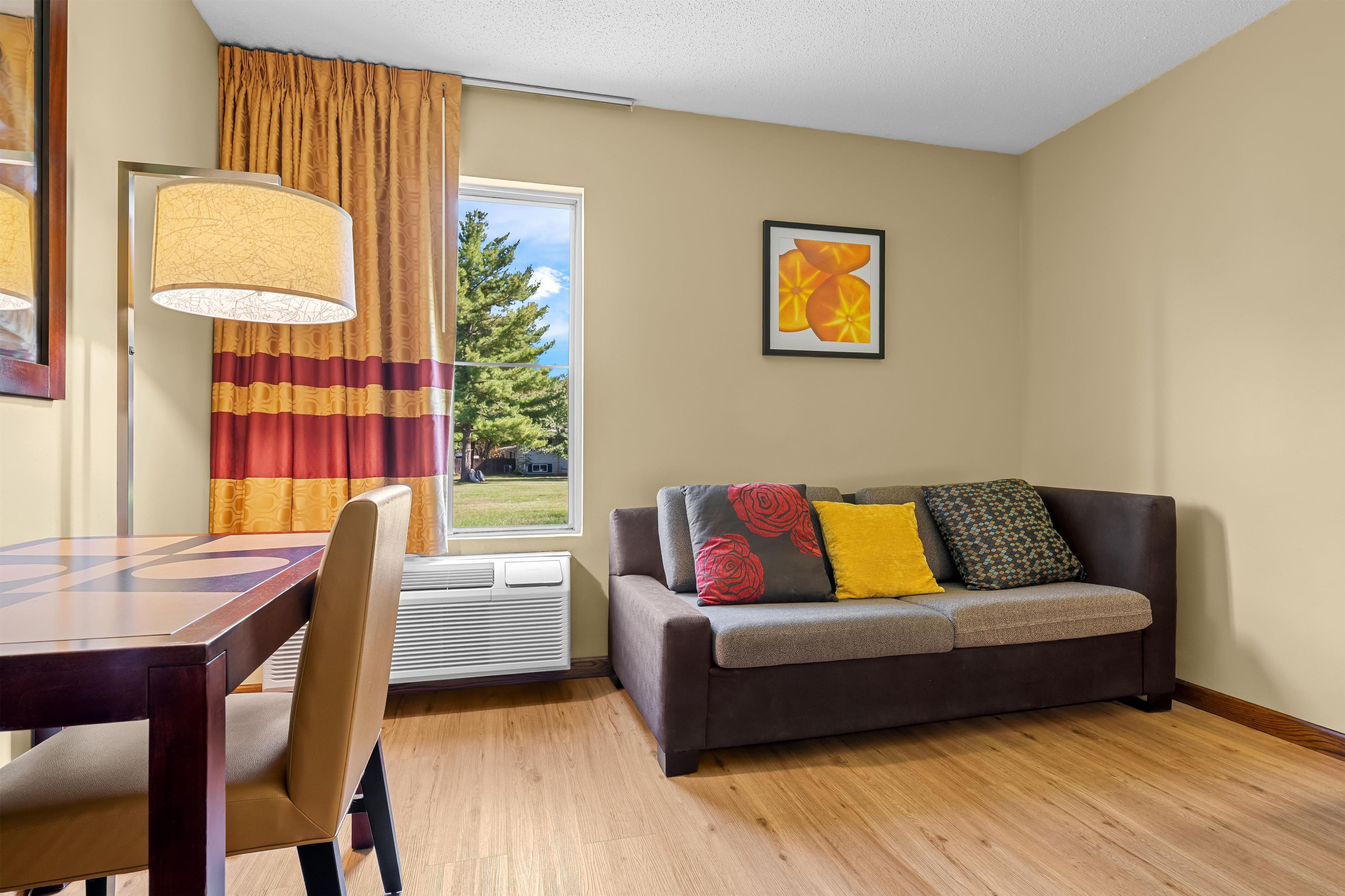 A room with a dining table, a sofa with cushions, a window with curtains, and a framed picture on the wall.