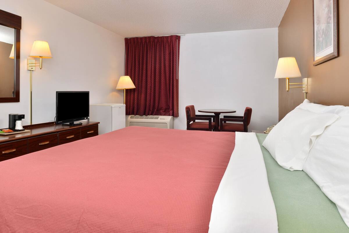 Une chambre d’hôtel avec un grand lit, un bureau avec une télévision, une chaise et deux lampes.