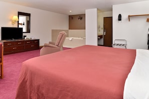 A hotel room with a large bed, a chair, a desk with a television, a bathroom with a bathtub, and a coat rack. - Americas Best Value Inn Beardstown (Beardstown)