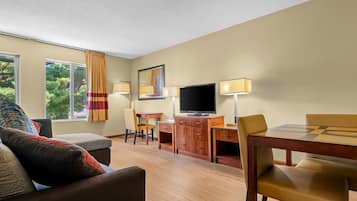 A hotel room with a sofa, a dining table, a TV, and a desk with a lamp.