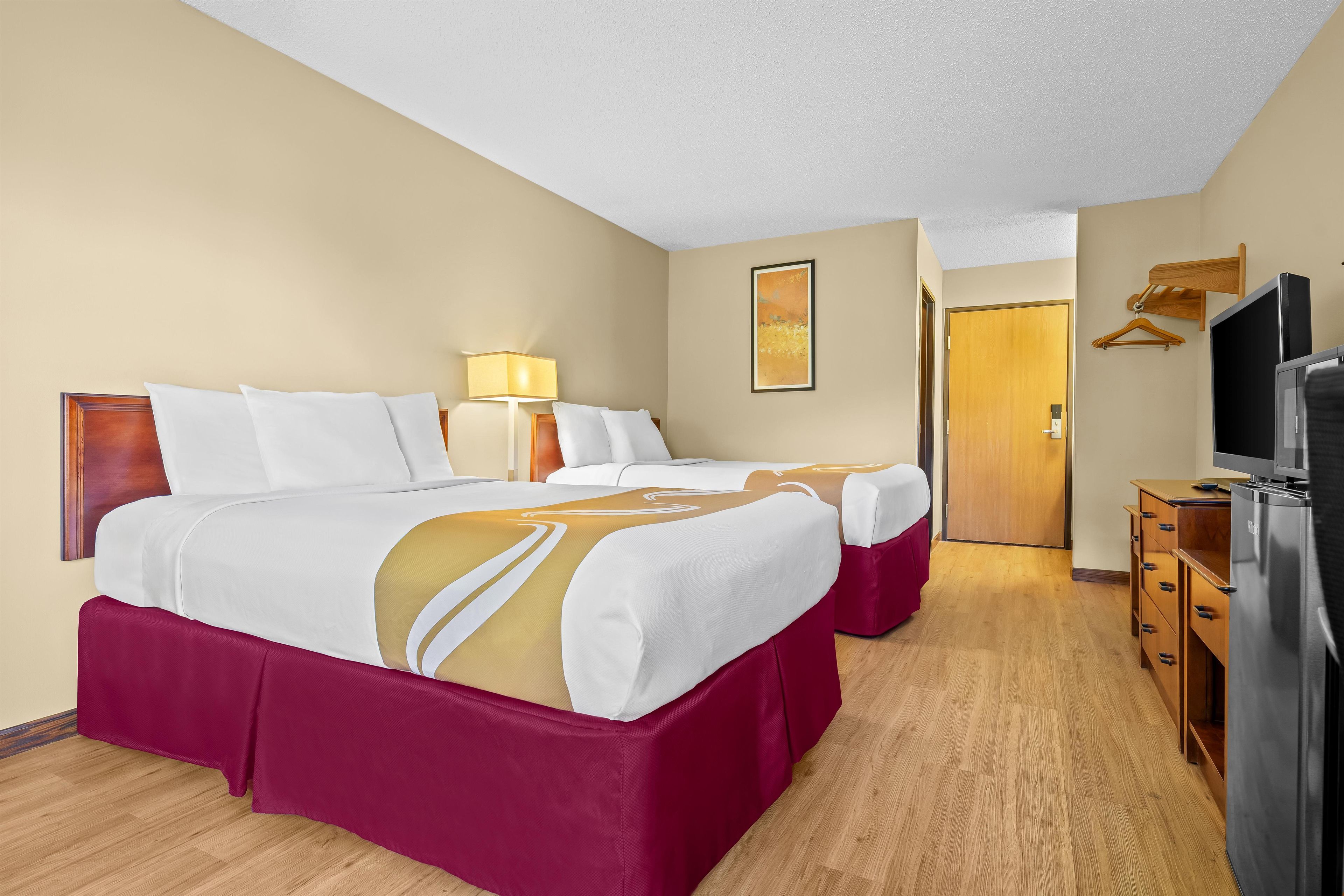 A hotel room with two beds, a television, a wooden dresser, and a door leading to another room.