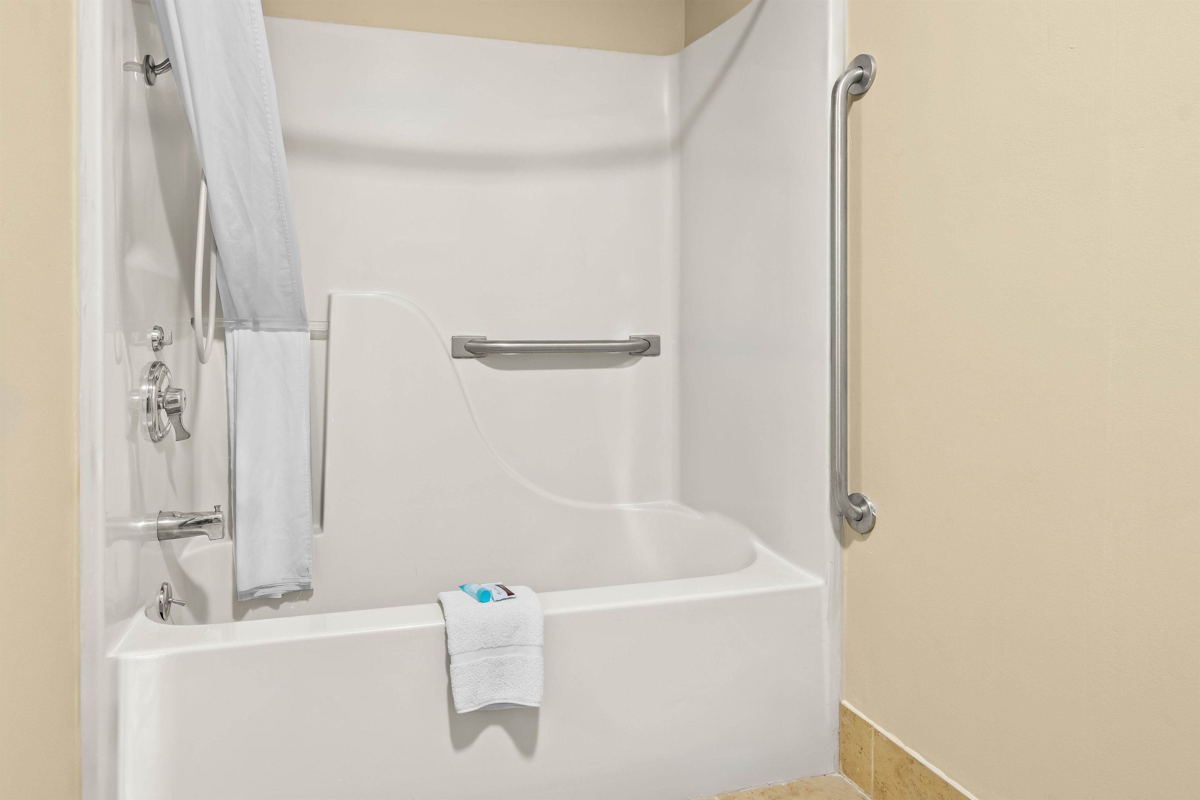 Eine weiße Badewanne mit Handlauf, Handtuchhalter und Duschvorhang.