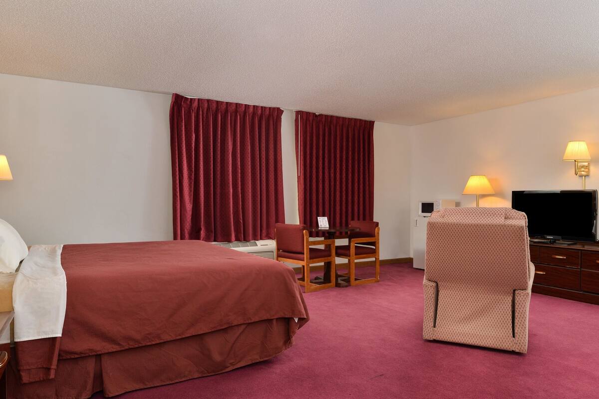 Une chambre d’hôtel comprenant un lit, un bureau avec une chaise, une télévision et deux lampes.