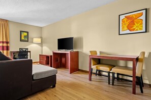 A hotel room with a sofa, a desk with a chair, a television, a lamp, and a painting on the wall. - Americas Best Value Inn Beardstown (Beardstown)