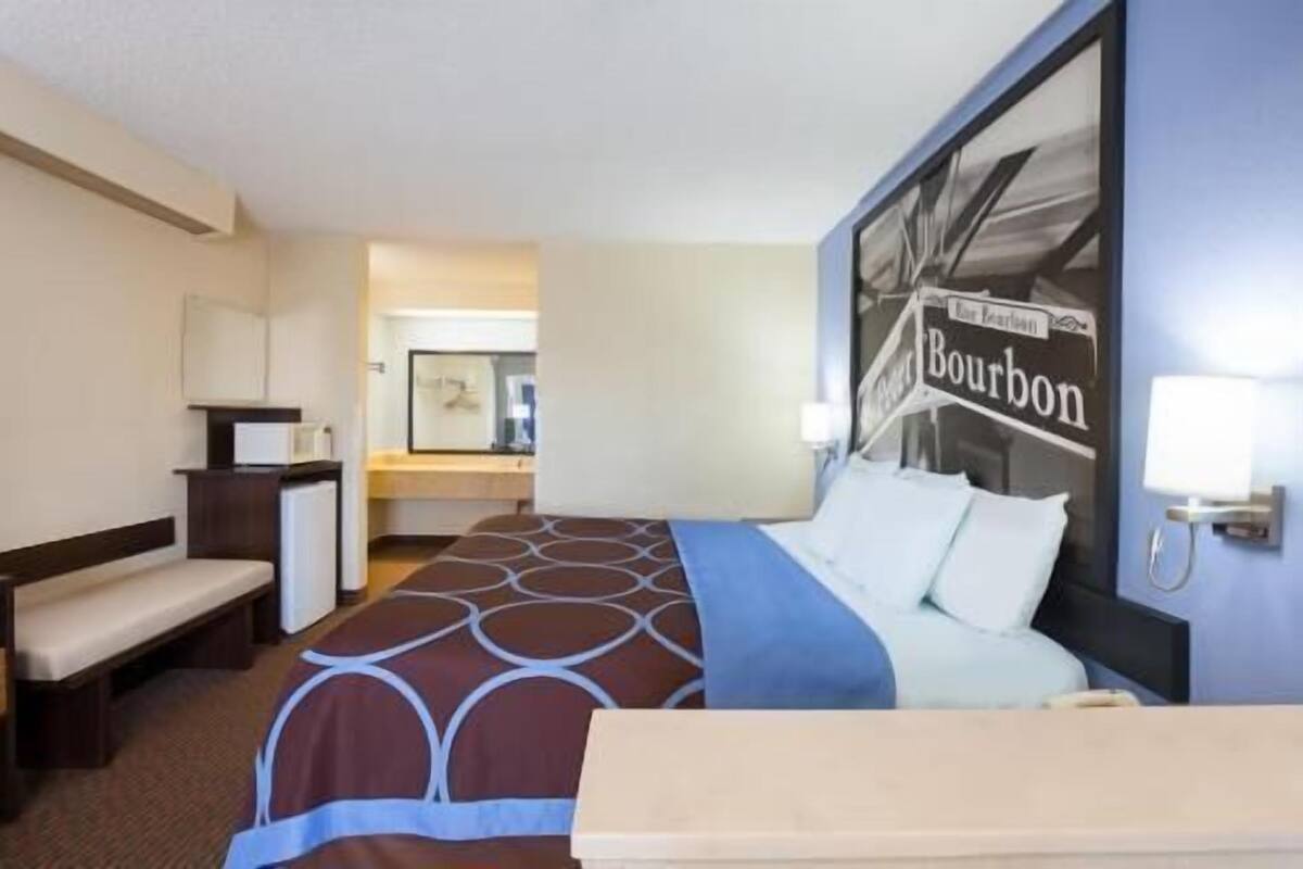 A hotel room with a bed, a desk, a chair, a mirror, and a wall with a Bourbon sign.
