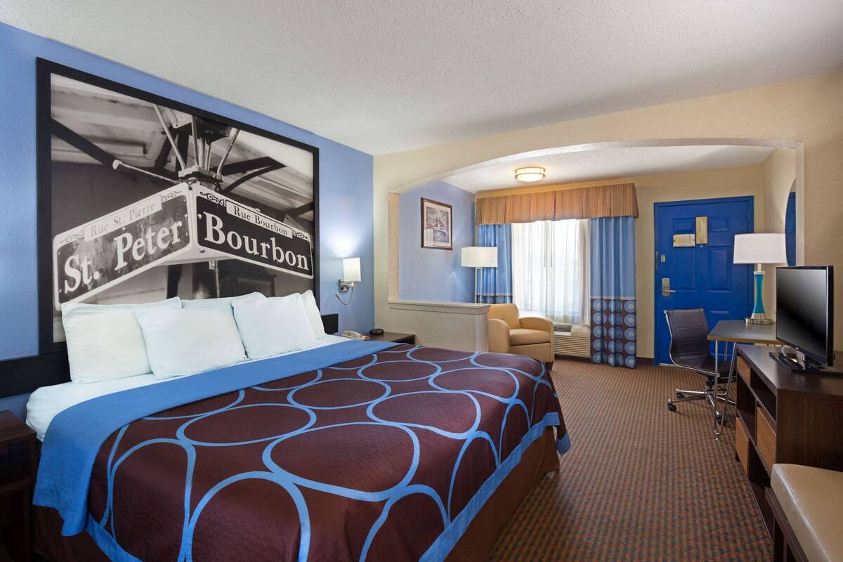 A hotel room with a large bed, a desk with a television, a chair, and a window with curtains.