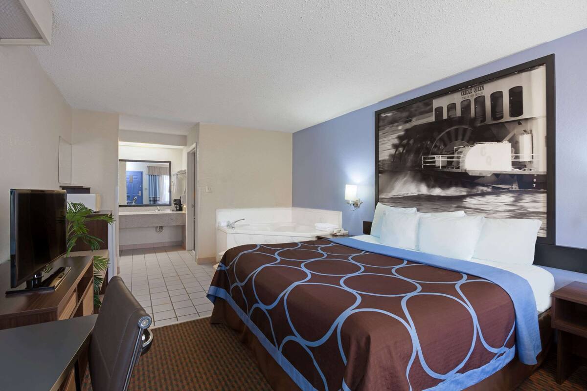A hotel room with a large bed, a desk with a TV, a bathroom with a bathtub, and a mural on the wall.