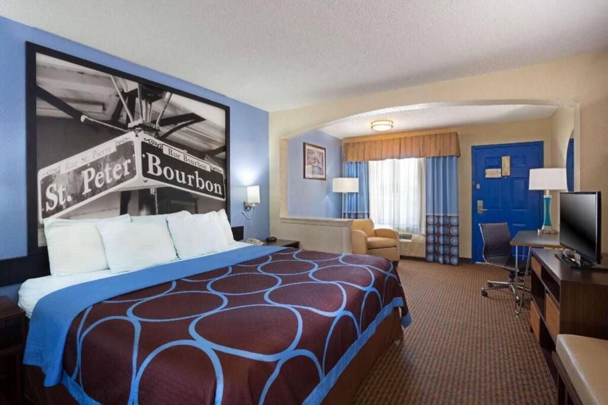 A hotel room with a large bed, a desk with a TV, a chair, and a door.