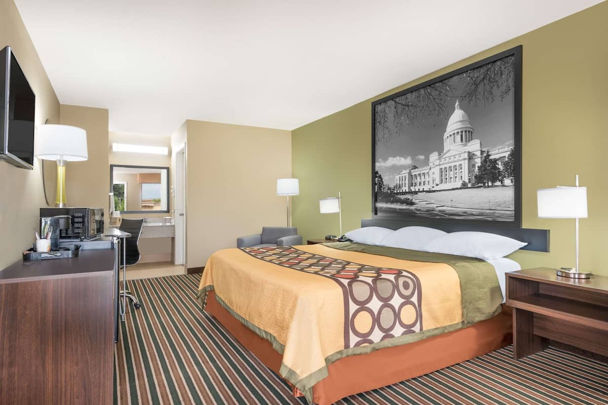 Ein Hotelzimmer mit einem großen Bett, einem Schreibtisch, einem Fernseher und einem gerahmten Bild eines Gebäudes.