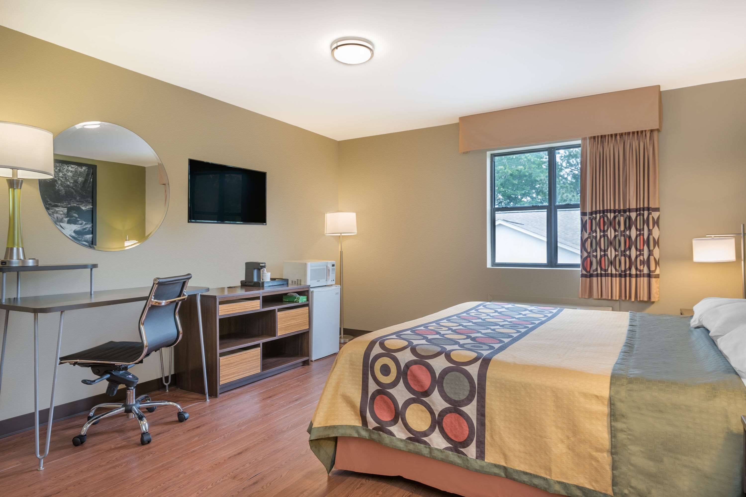 Une chambre d’hôtel avec un lit, un bureau, une chaise et une grande fenêtre.