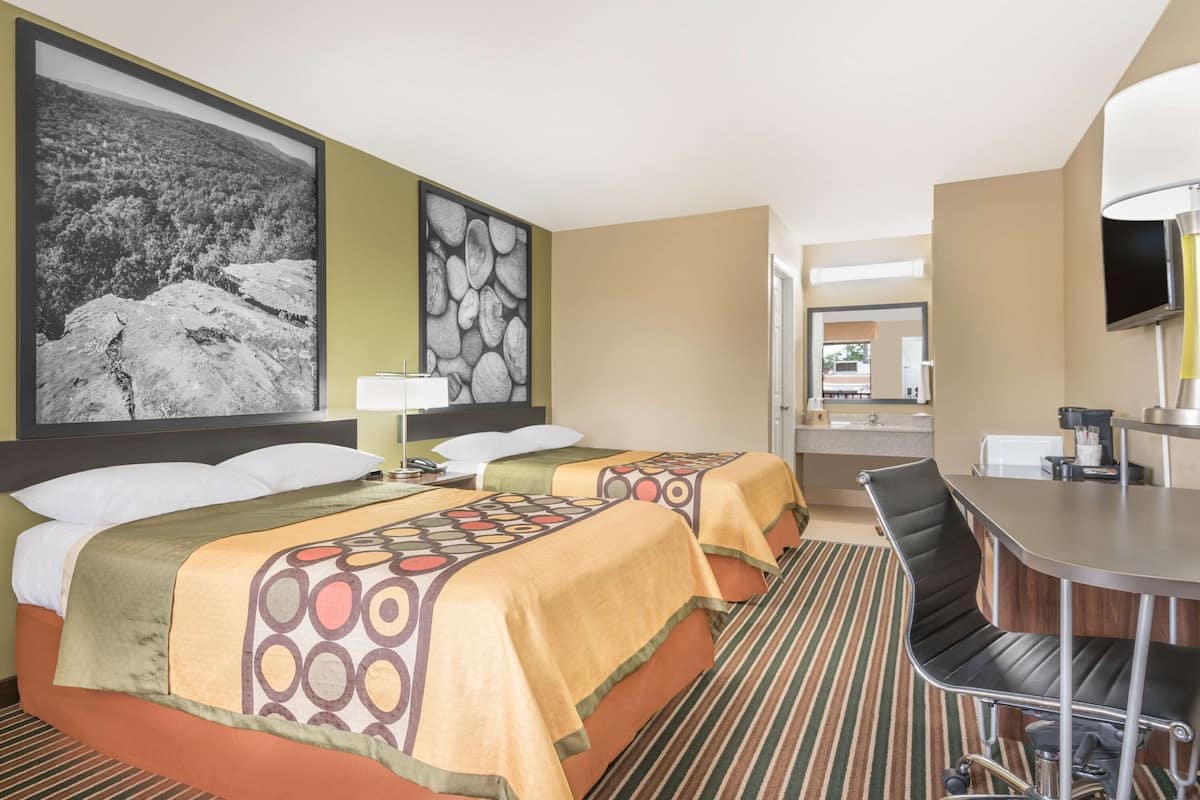 Ein Hotelzimmer mit zwei Betten, einem Schreibtisch, einem Stuhl, einem Fernseher und Bildern an den Wänden.