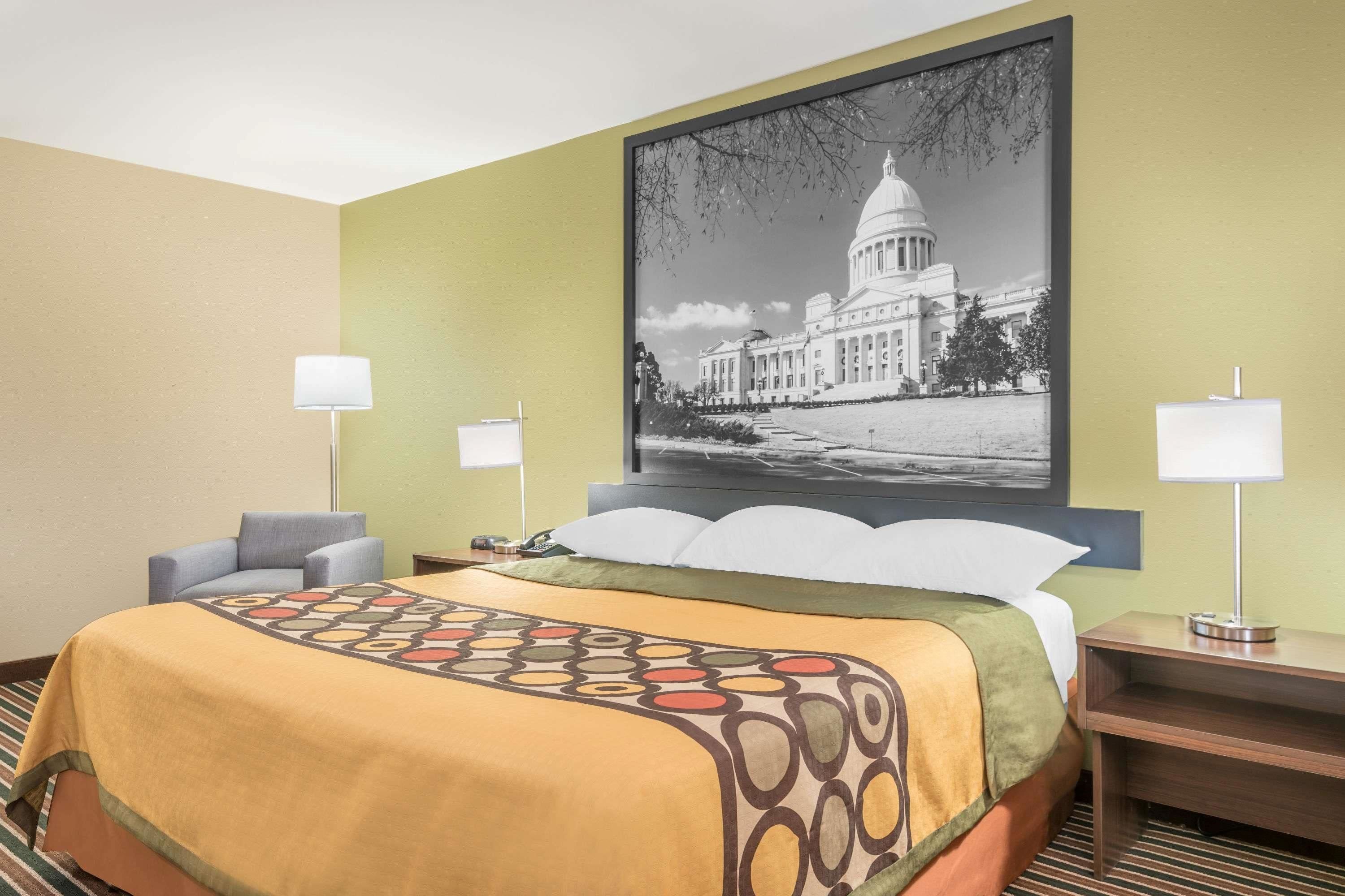 Habitación de hotel con una cama grande, dos lámparas de noche, una mesita de noche y un cuadro con una imagen de un edificio en la pared.