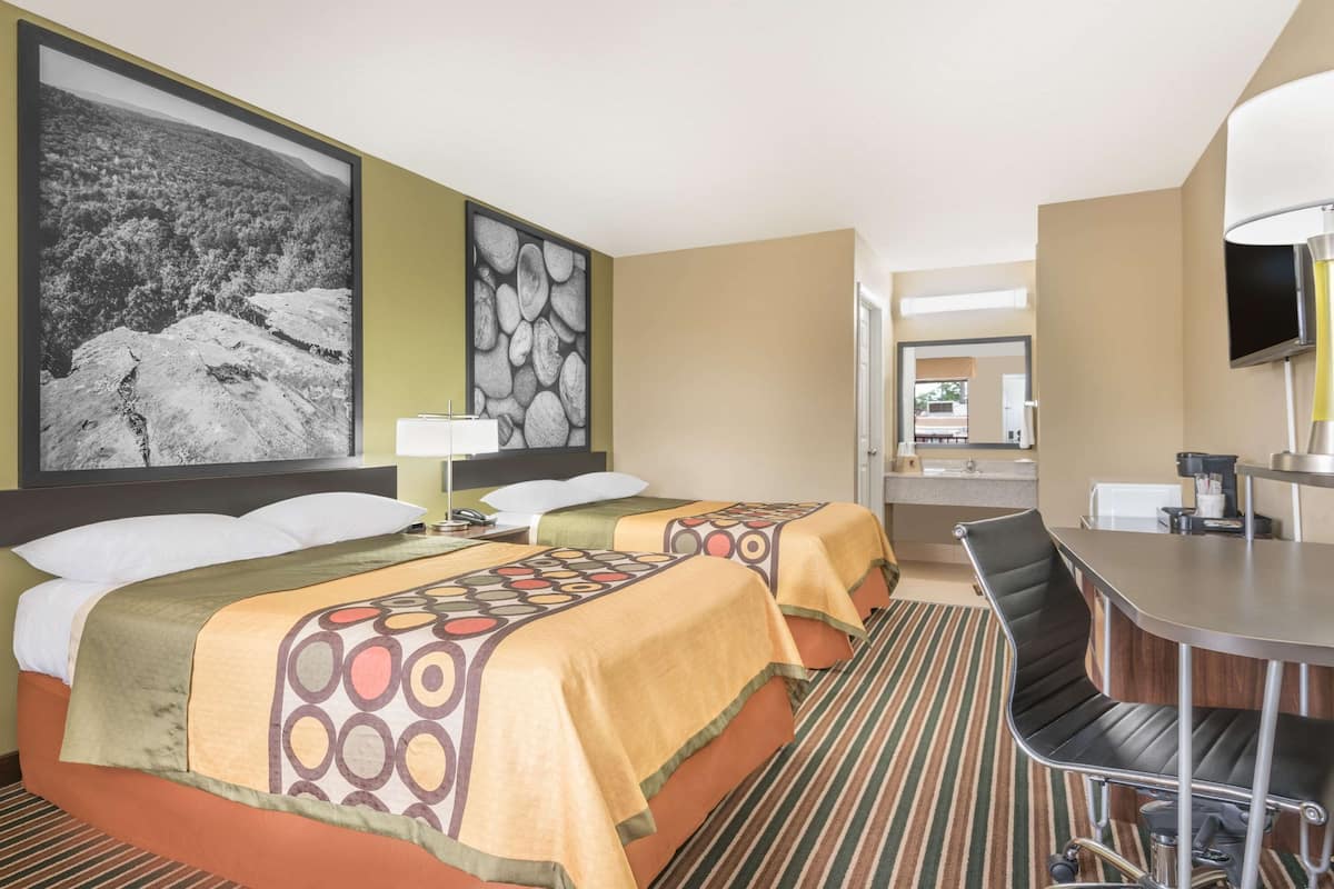 Ein Hotelzimmer mit zwei Betten, einem Schreibtisch, einem Sessel, einem Fernseher und einem großen Gemälde an der Wand.