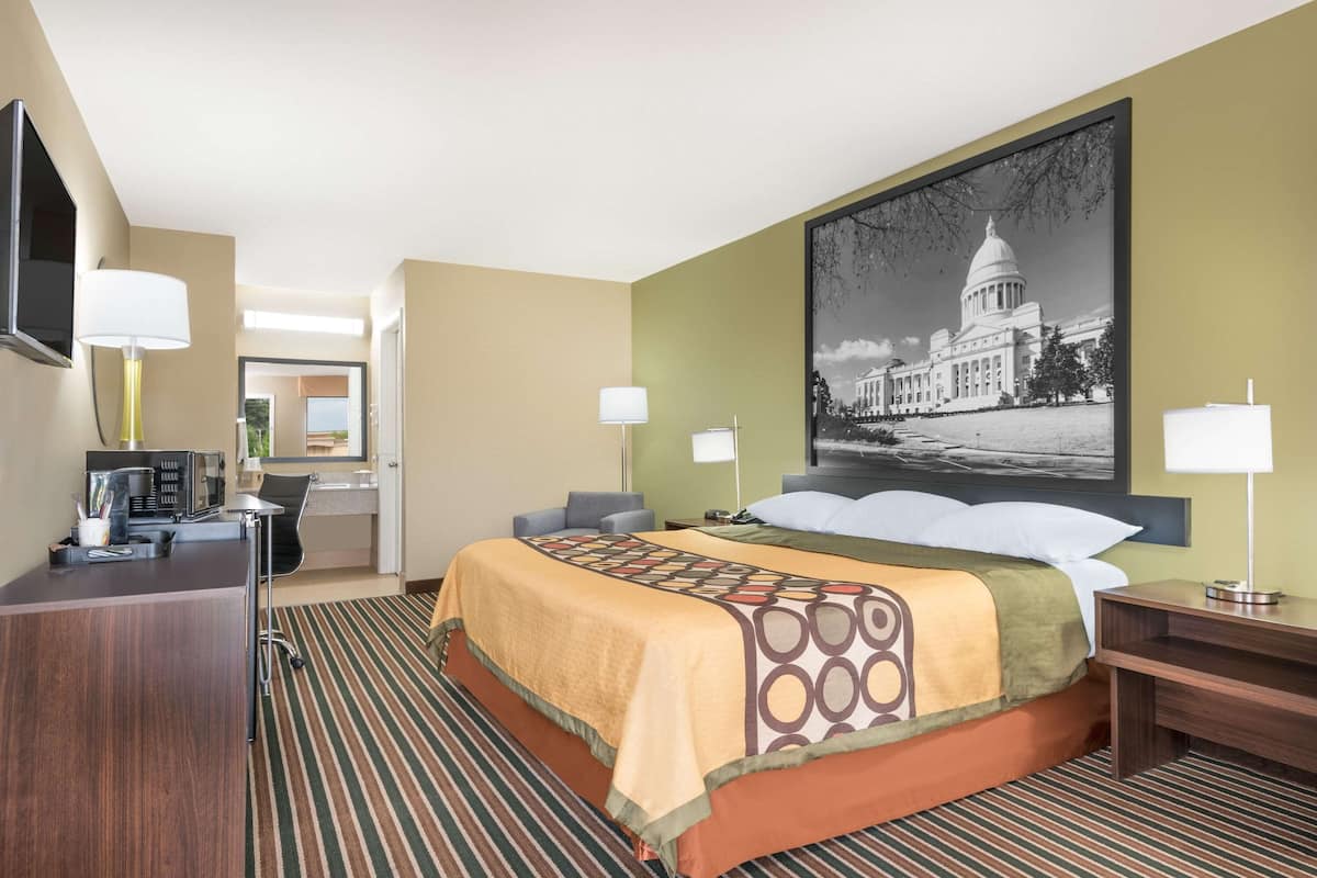 Ein Hotelzimmer mit einem großen Bett, einem Schreibtisch, einem Sessel, einem Fernseher und einem gerahmten Bild eines Gebäudes.