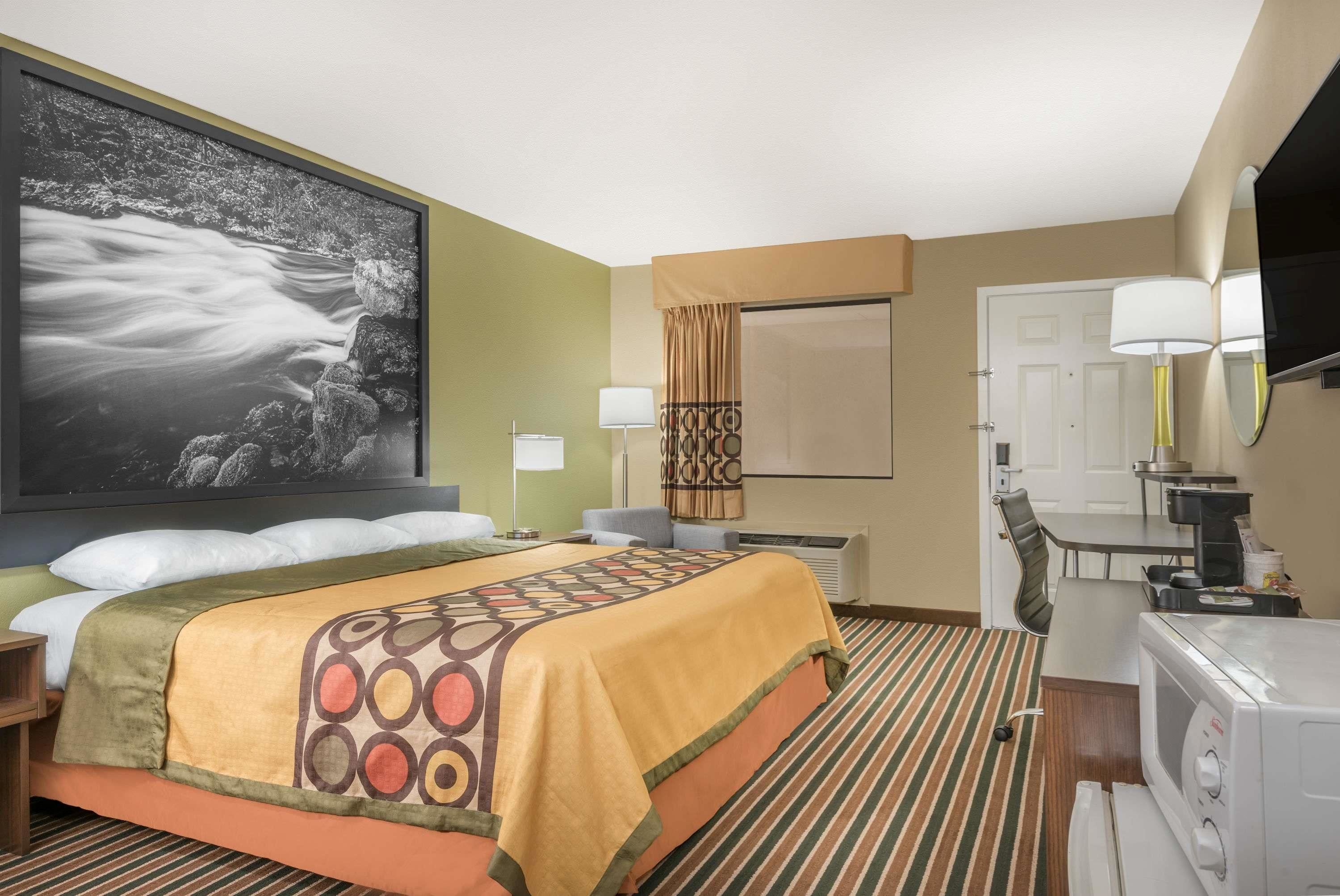 A hotel room with a large bed, a flat-screen TV, a microwave, a dining table, and a large framed picture of a river.