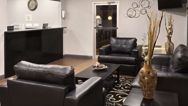 A modern lobby with a reception desk, leather seating, a decorative vase, and a wall-mounted clock. - Super 8 by Wyndham Ardmore (Ardmore)