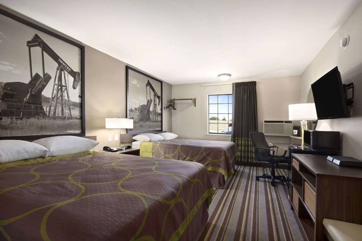 A hotel room with two beds, a desk, a television, and a window with curtains.