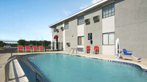 A swimming pool with a metal ladder, red and white lounge chairs, and a building with windows and air conditioning units. - Super 8 by Wyndham Ardmore (Ardmore)