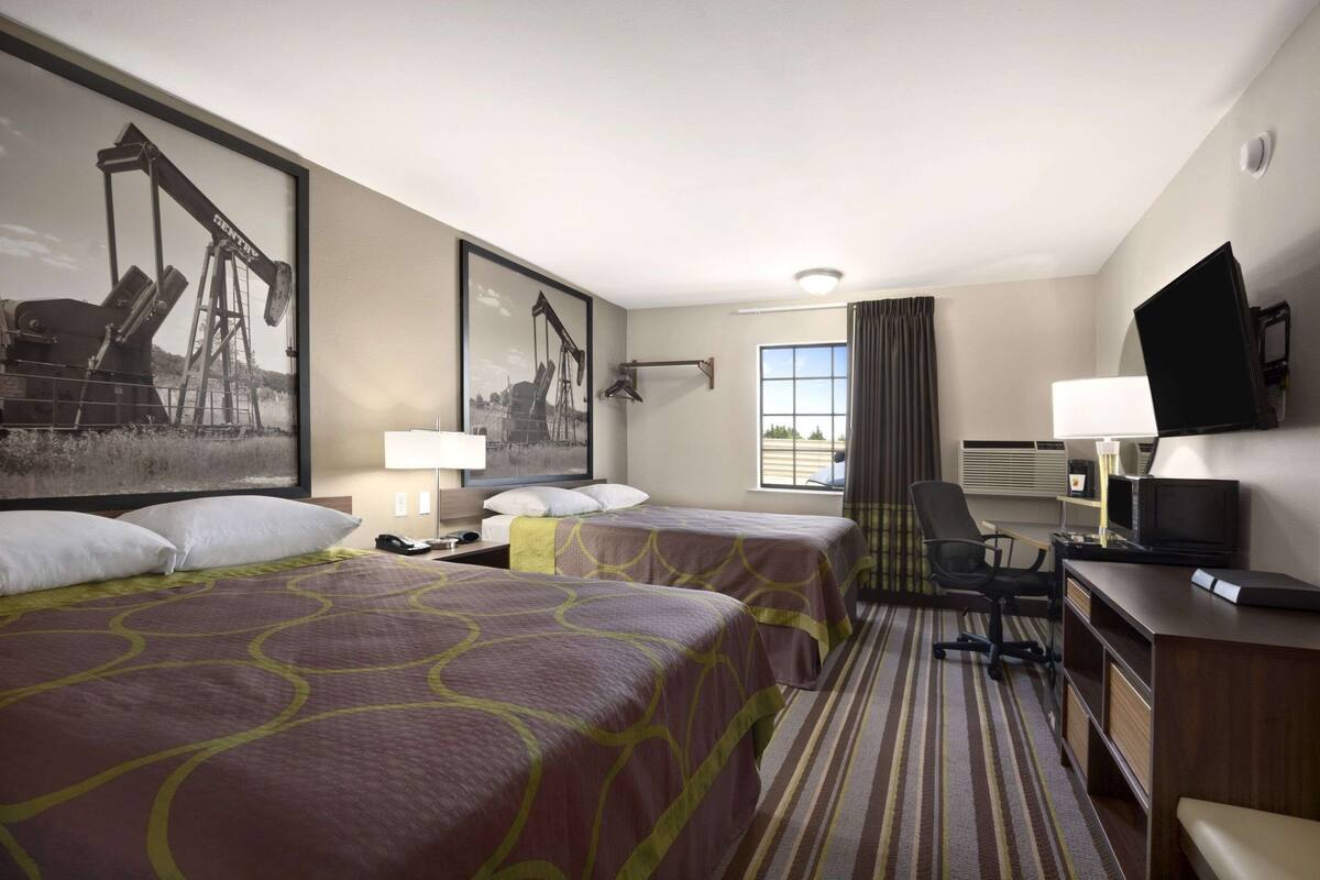 A hotel room with two beds, a desk, a chair, a television, and a window with curtains.
