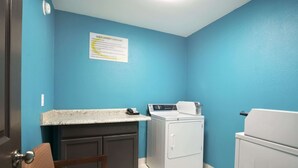 A laundry room with a blue wall, a washing machine, a dryer, a countertop with a phone, and a cabinet. - Super 8 by Wyndham Ardmore (Ardmore)