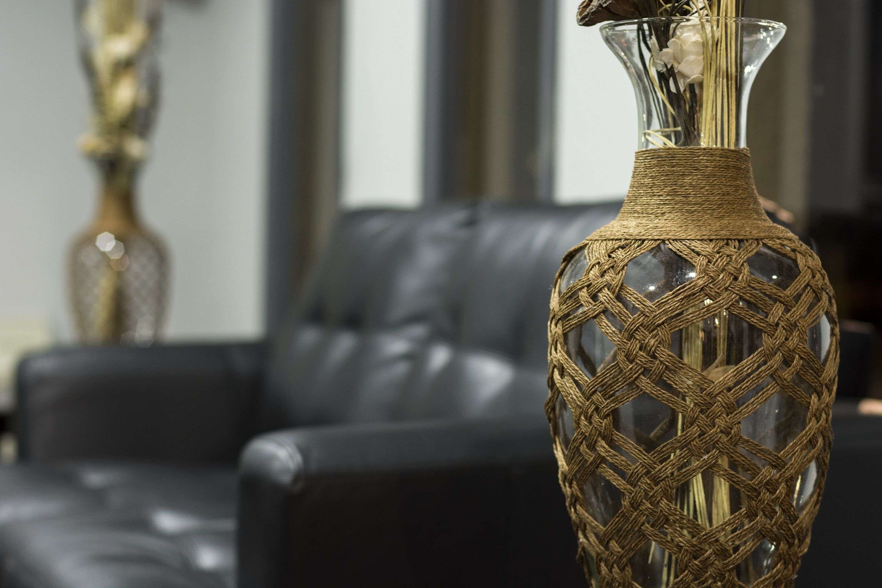 A clear view of a woven vase with a textured pattern, placed on a dark leather couch.