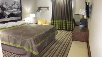 A hotel room with a bed, a chair, a desk, a television, and a window with curtains.