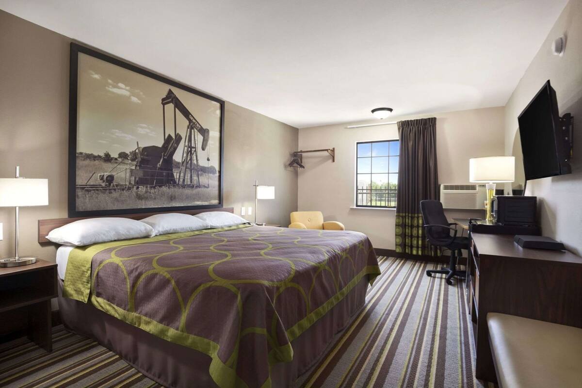 A hotel room with a large bed, a desk with a chair, a television, and a window with curtains.