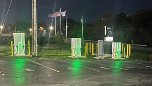 Un estacionamiento con estaciones de carga para vehículos eléctricos, un asta con la bandera estadounidense y un letrero que indica Orbits Inn.