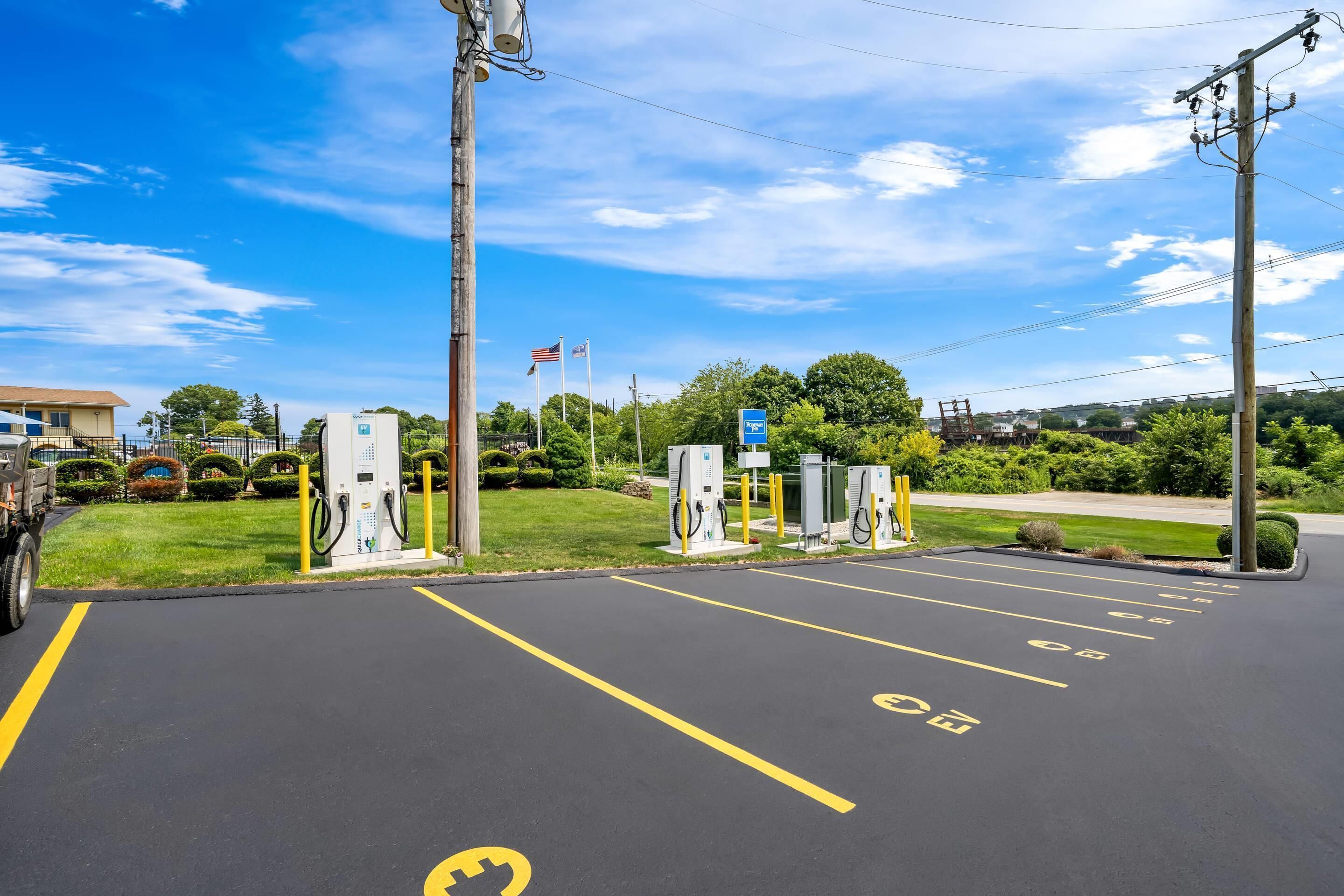 A parking lot with electric vehicle charging stations, a hotel sign, and a flag.