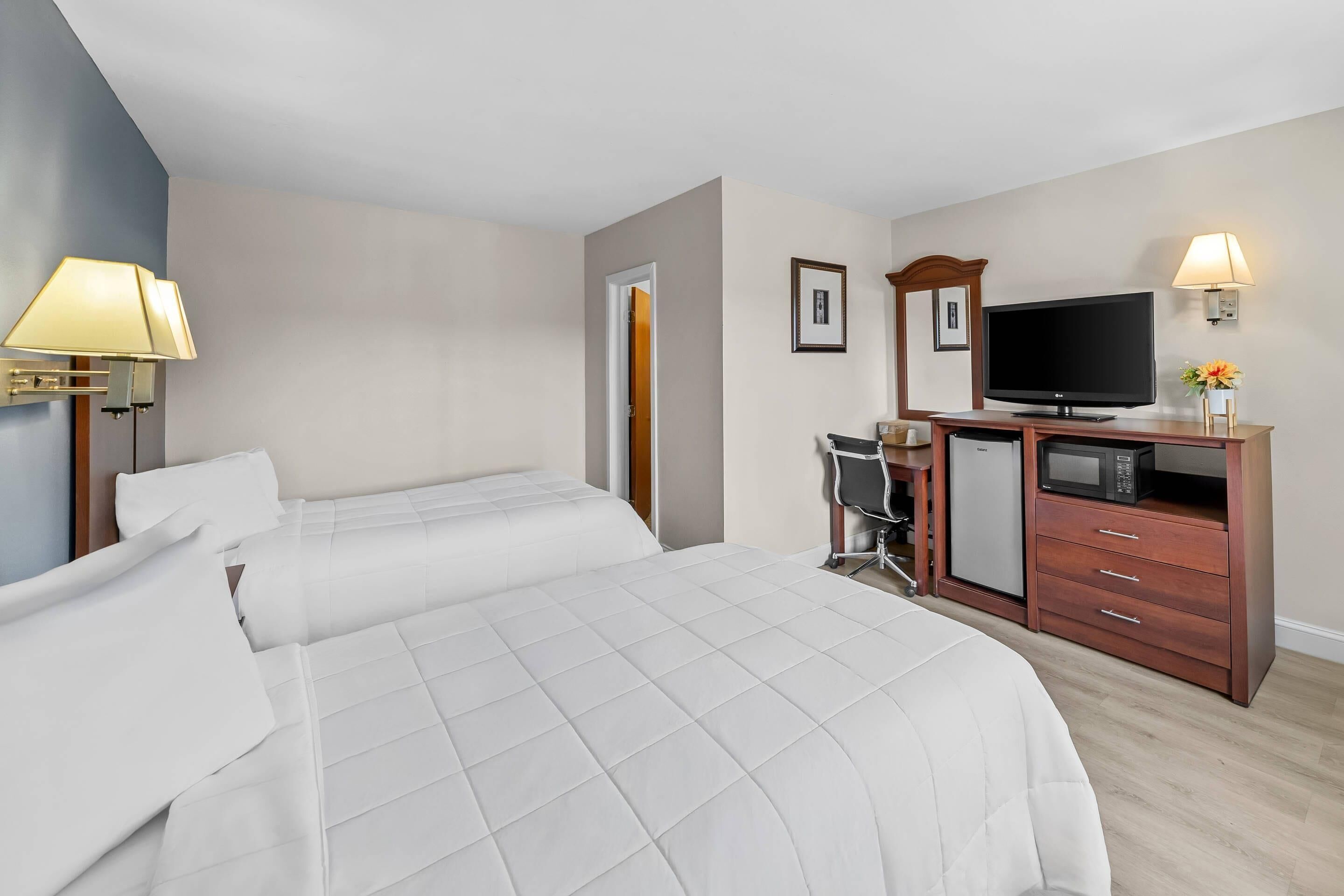 Quarto de hotel com duas camas, uma escrivaninha com cadeira, televisão, micro-ondas e frigorífico.