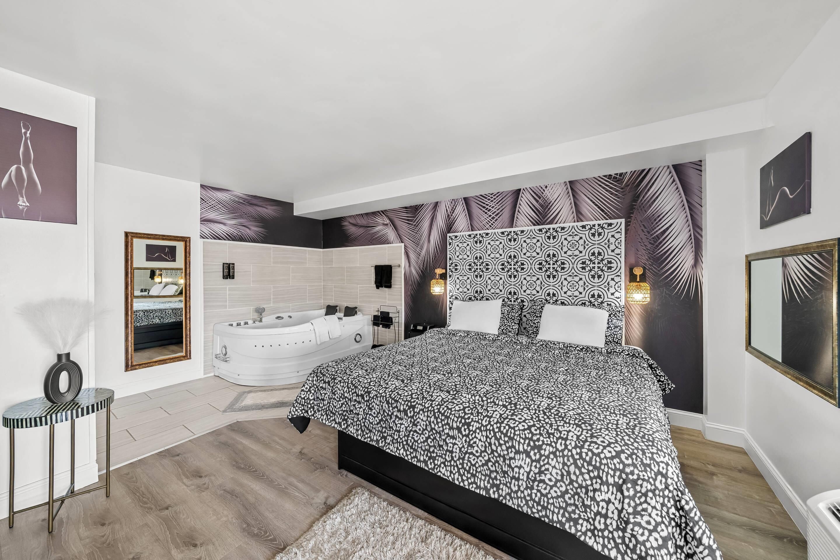 A modern bedroom with a large bed, a separate bathroom with a bathtub, and a view of the city.