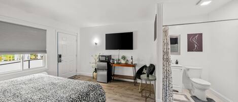 Un dormitorio moderno con una cama, un escritorio con televisor de pantalla plana, un refrigerador y una silla.