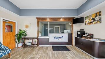 A reception area with a reception desk, a coffee station, and a seating area with a sofa and plants.