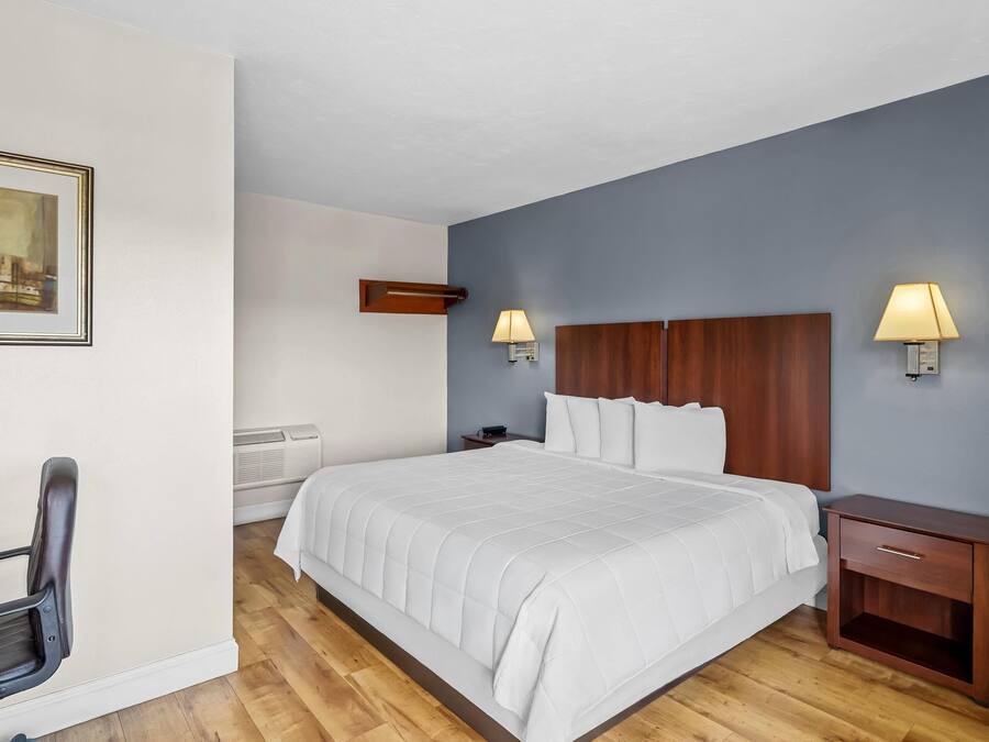 A hotel room with a bed, bedside tables, a chair, and a painting on the wall.