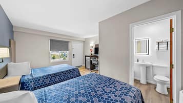 A hotel room with two beds, a desk, a chair, a window with a view, a kitchenette, and a bathroom.