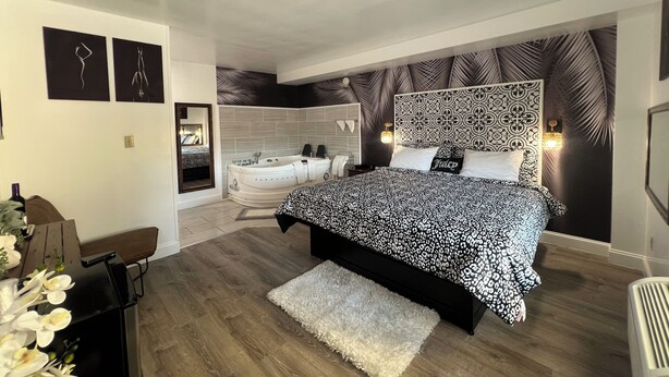 Un dormitorio moderno con una cama grande, una bañera integrada y un cabecero decorativo.