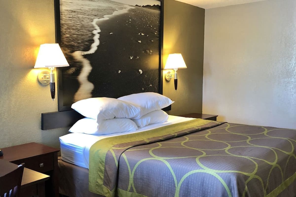 Una habitación de hotel con una cama, dos lámparas de pared, un escritorio y una silla.