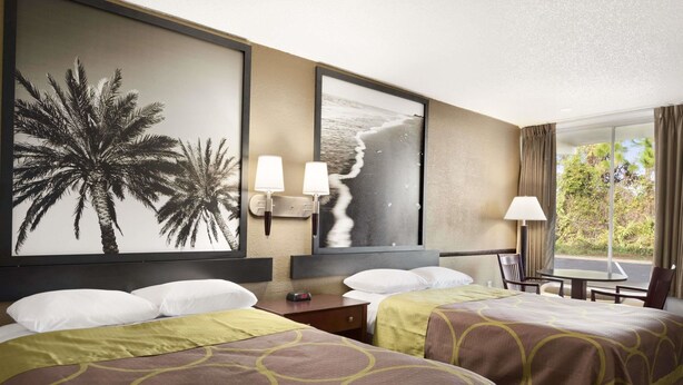 Habitación de hotel con dos camas, un mural grande en la pared, un televisor y una ventana con cortinas.