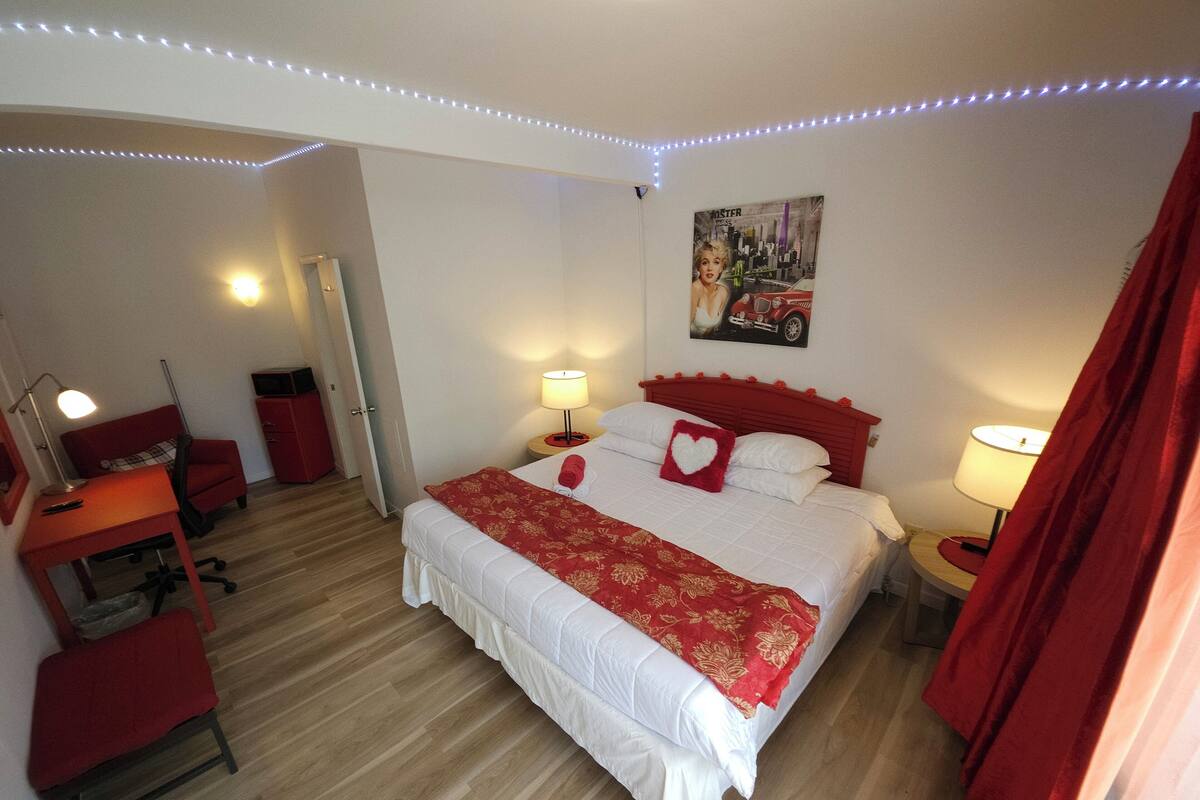 A hotel room with a bed, a desk, a chair, a lamp, and a painting on the wall.