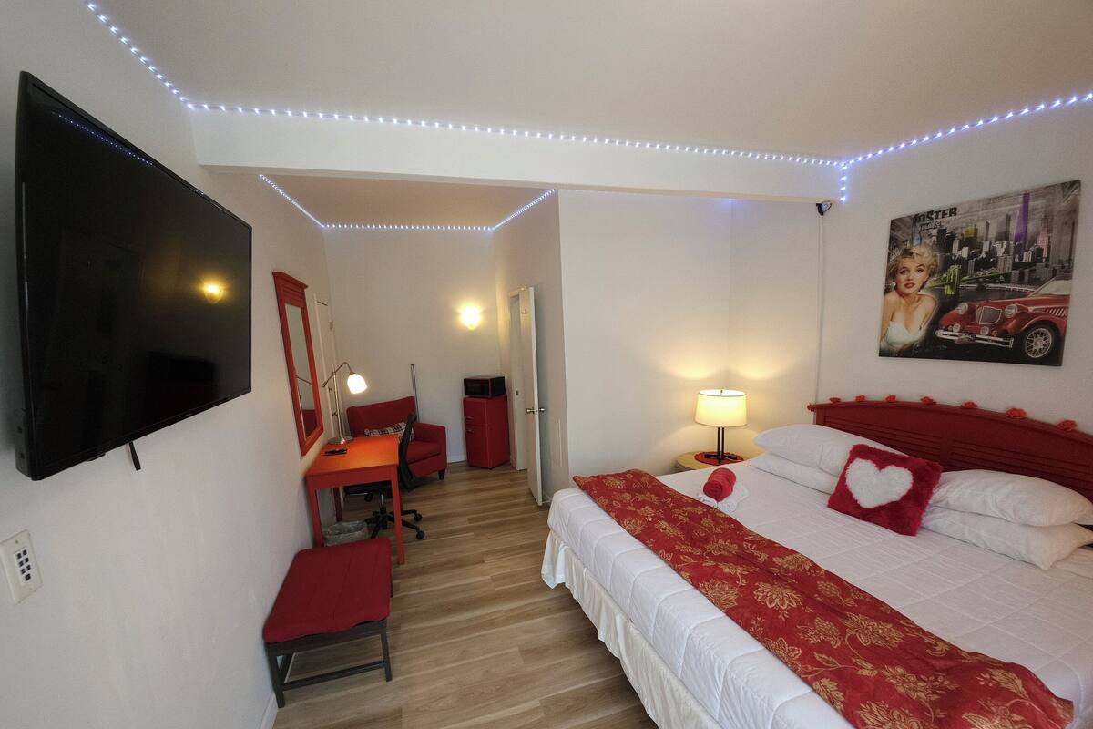 A hotel room with a bed, a desk, a chair, a TV, and a painting on the wall.