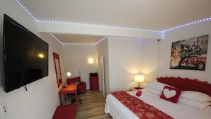 Habitación de hotel con cama, escritorio, silla, televisor y un cuadro en la pared.
