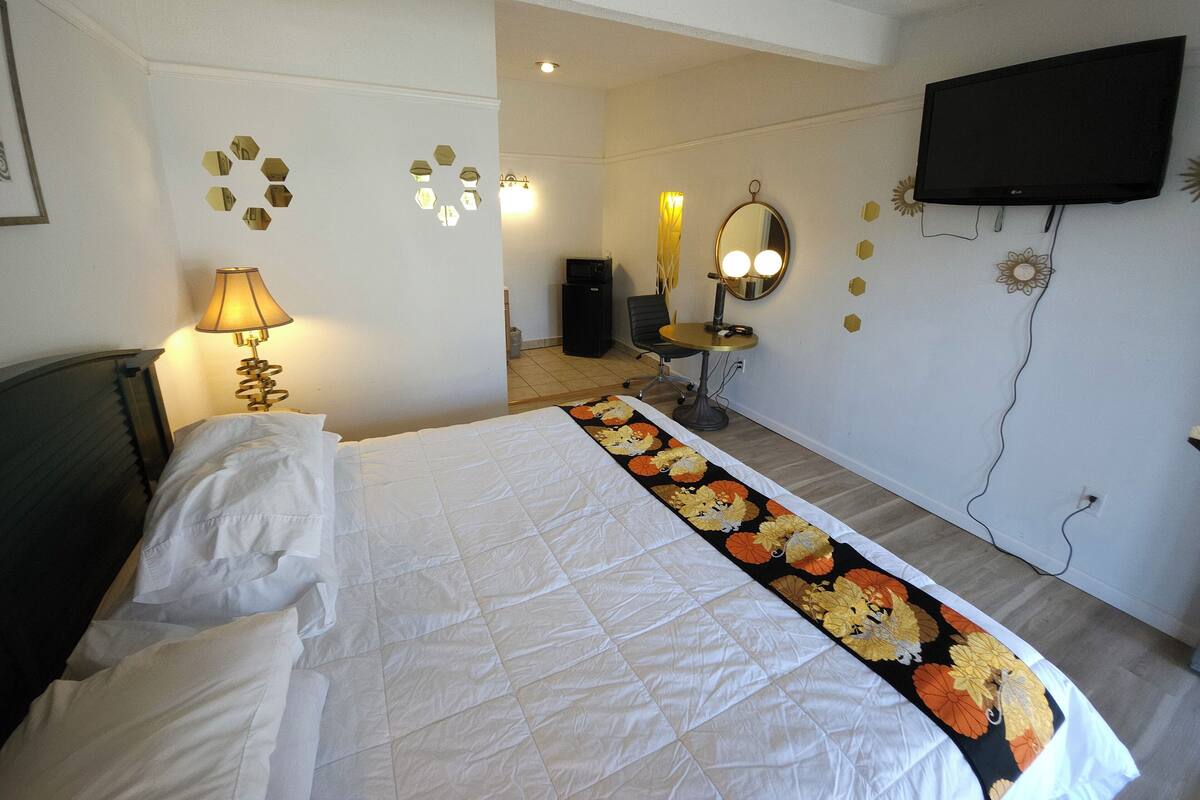 A hotel room with a bed, a desk with a mirror, a television, and a lamp.