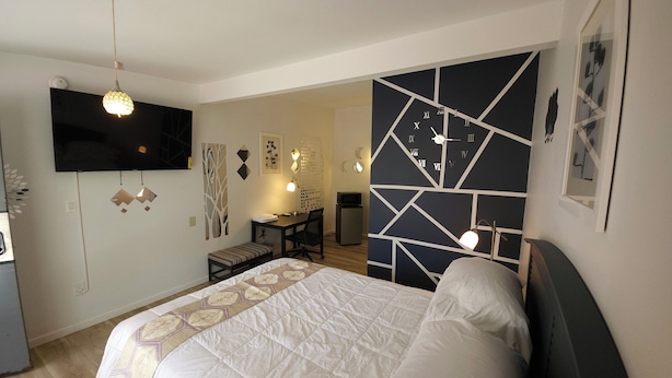 Un dormitorio con una cama, un escritorio, una silla, un televisor y un reloj de pared.