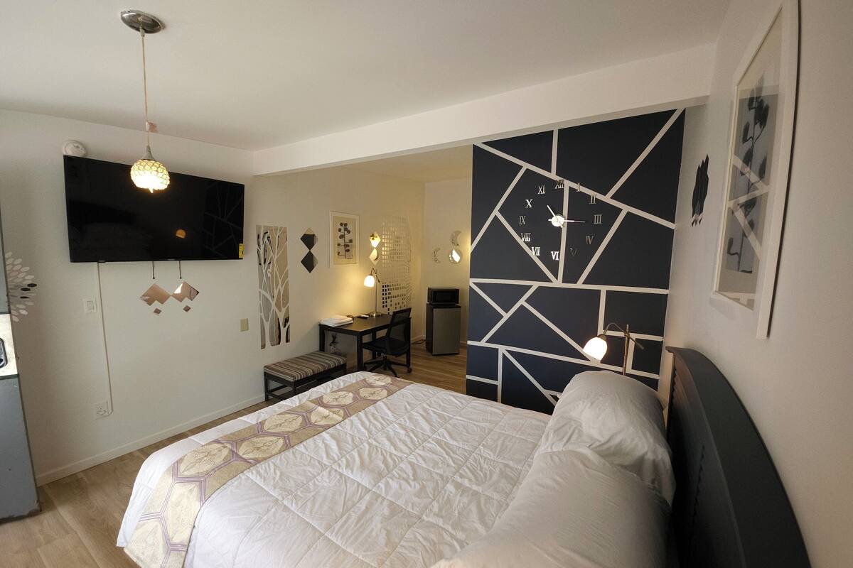 A bedroom with a bed, a desk, a chair, a TV, and a wall clock.