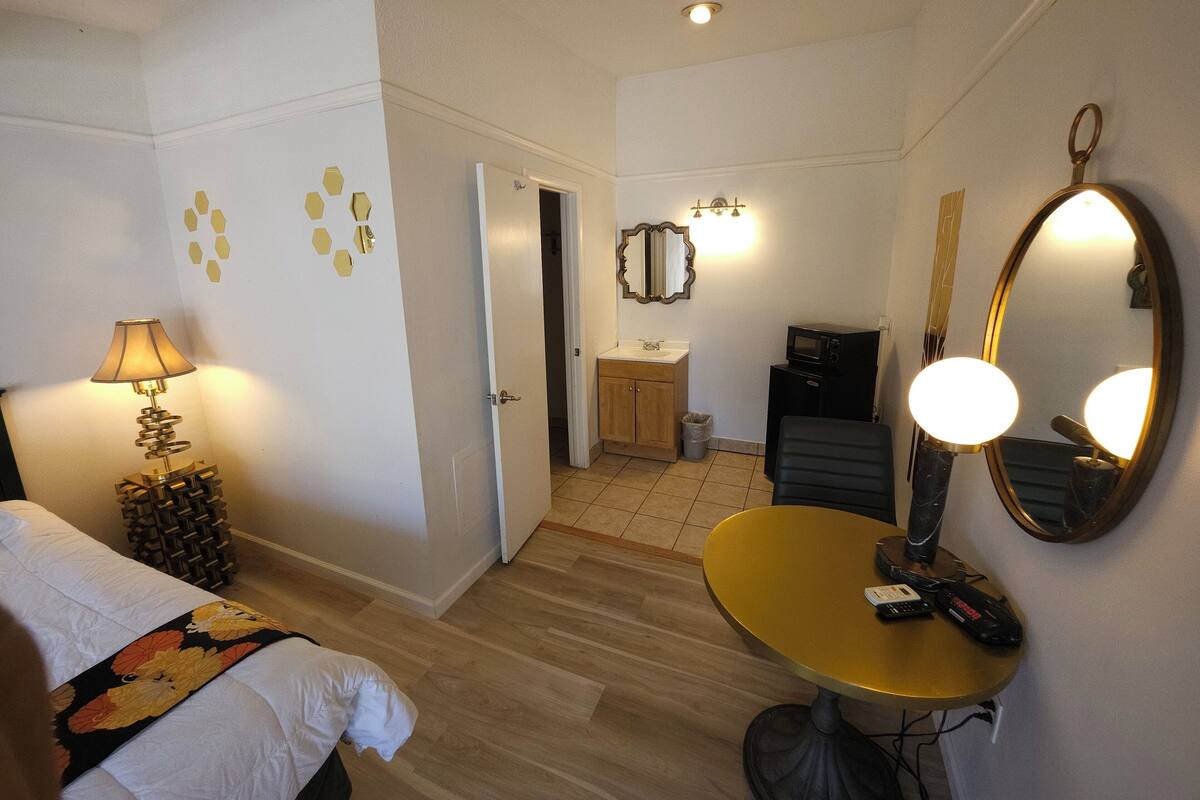 A hotel room with a bed, a bedside lamp, a small table with a mirror, a microwave, and a trash bin.