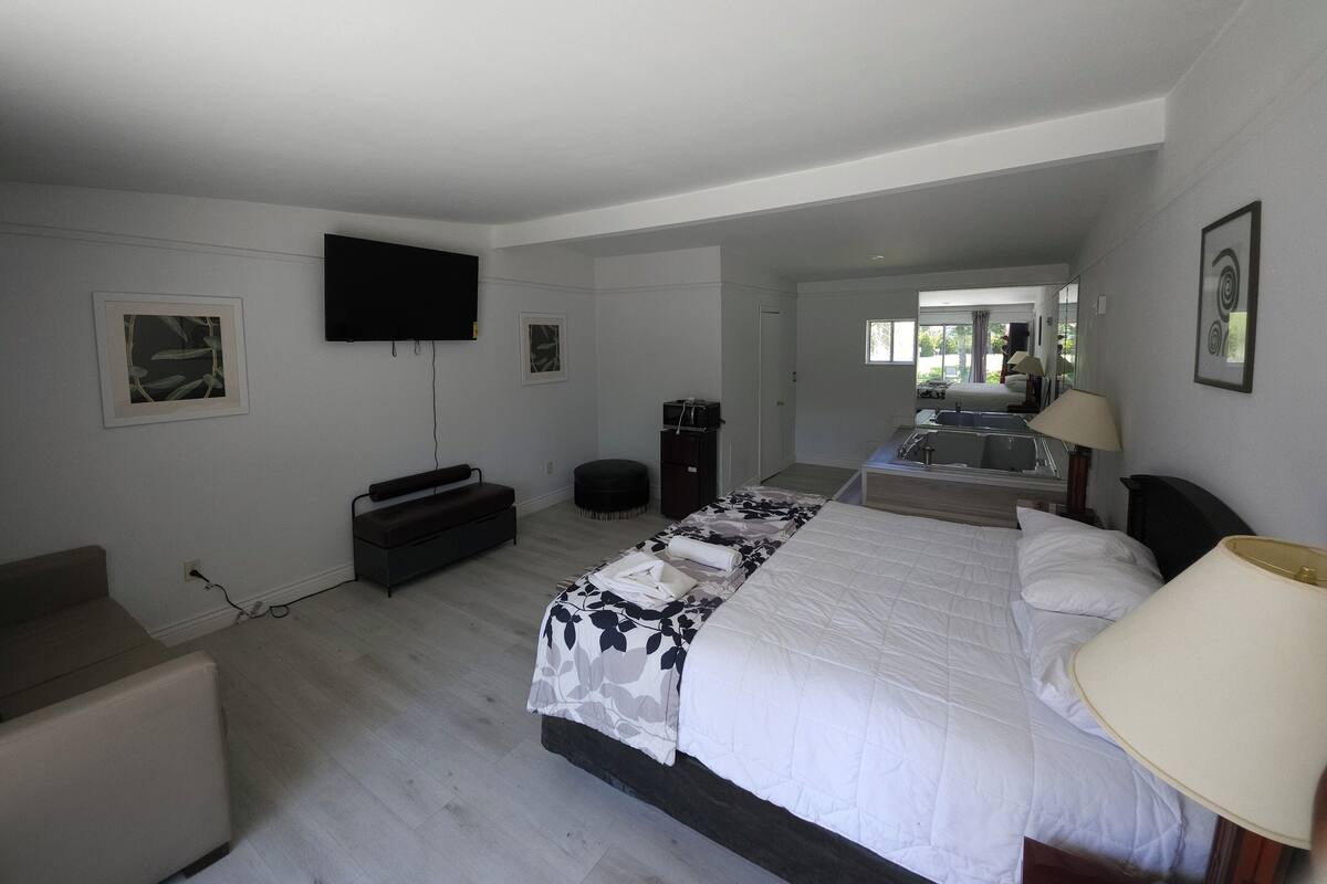 A bedroom with a large bed, a TV mounted on the wall, a desk, and a chair.