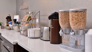 Une petite cuisine équipée d’une machine à café, d’un distributeur d’eau chaude et de deux grands récipients pour les céréales.