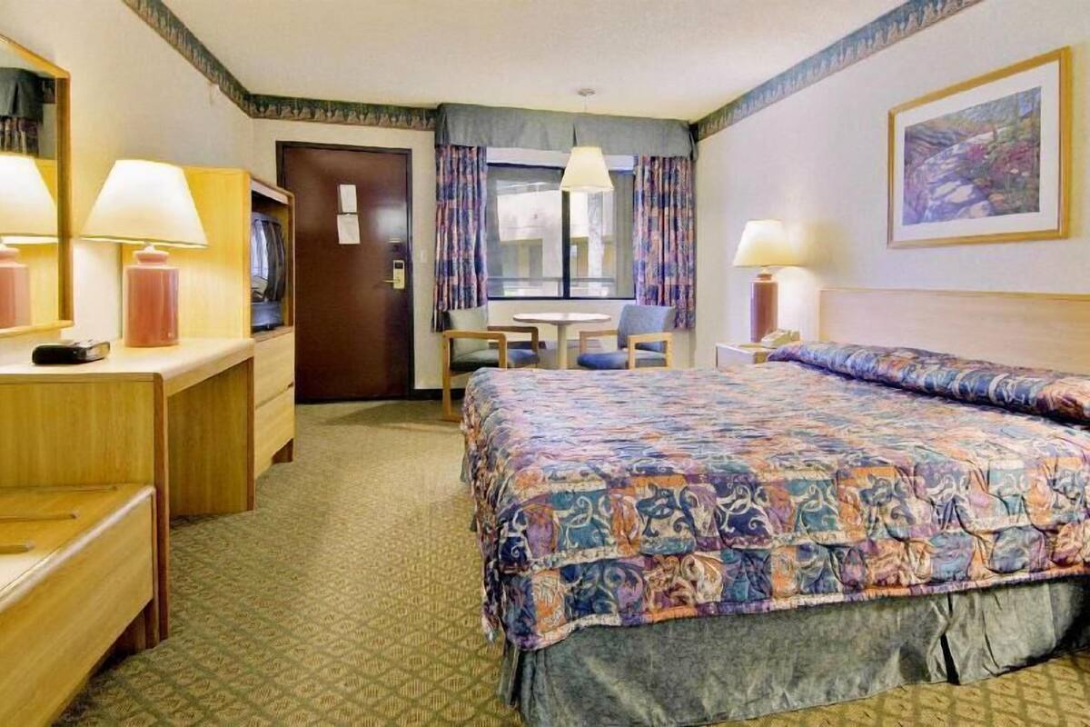 Habitación de hotel con cama, escritorio, silla, mesa y ventana con cortinas.