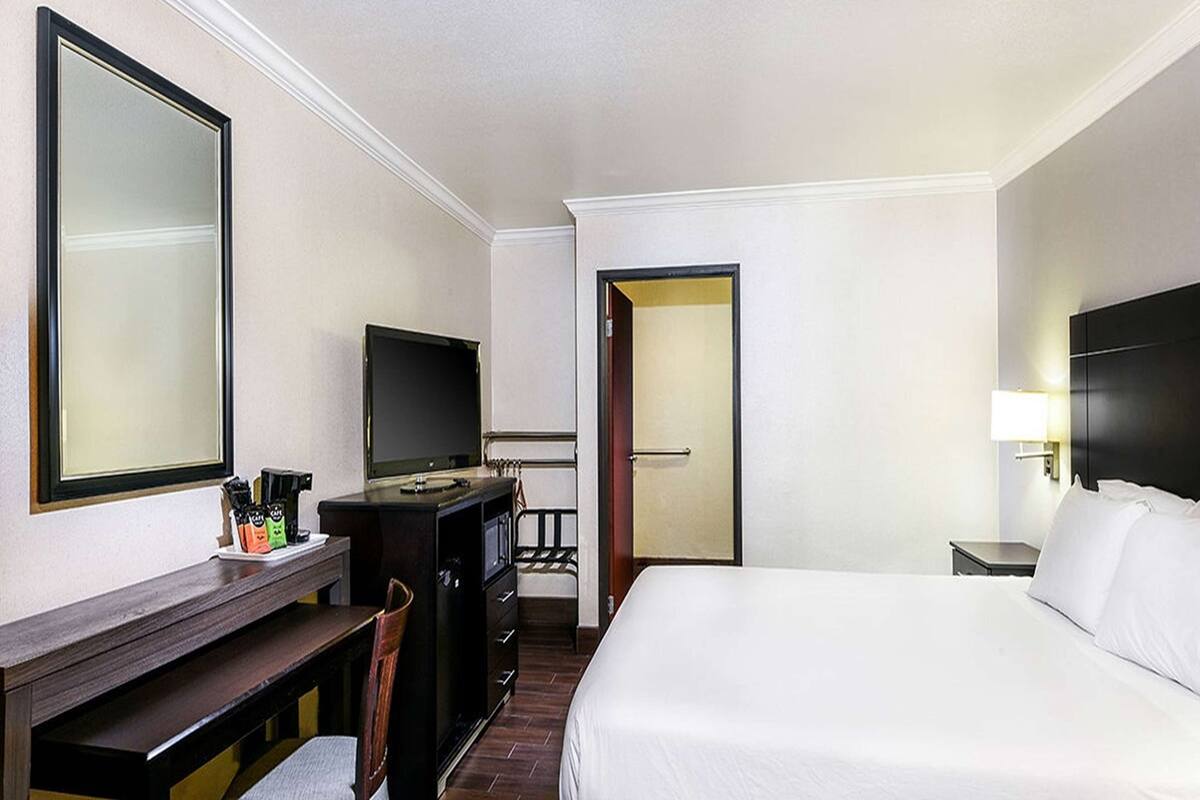 Habitación de hotel con cama, escritorio con silla, televisor, armario y puerta que da a otra habitación.