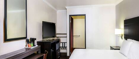 A hotel room with a bed, a desk with a chair, a television, a wardrobe, and a door leading to another room.